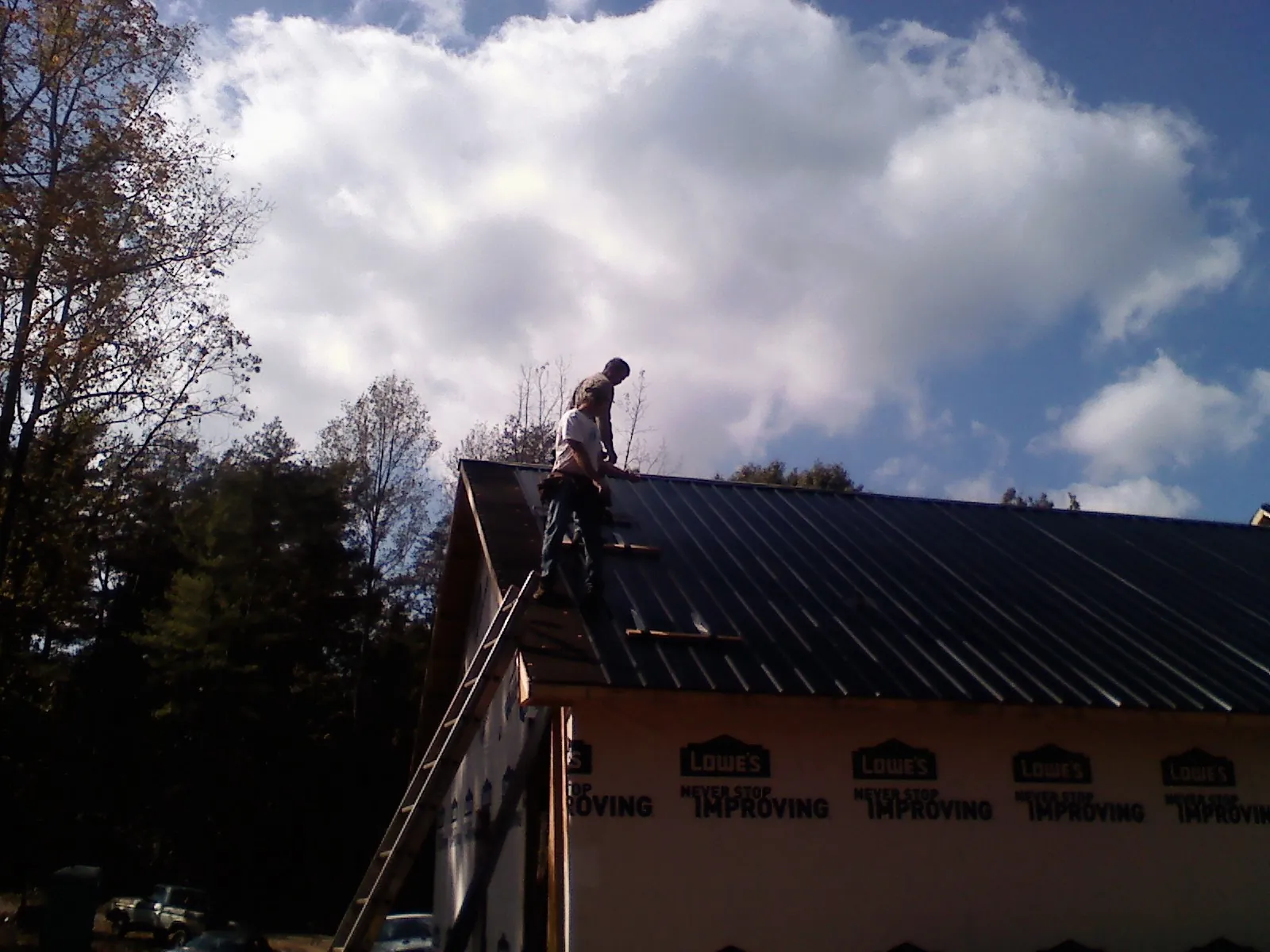 Roofer fastening dark metal panels high against a cloudy sky, from a Roof Inspection job in Issaquah
