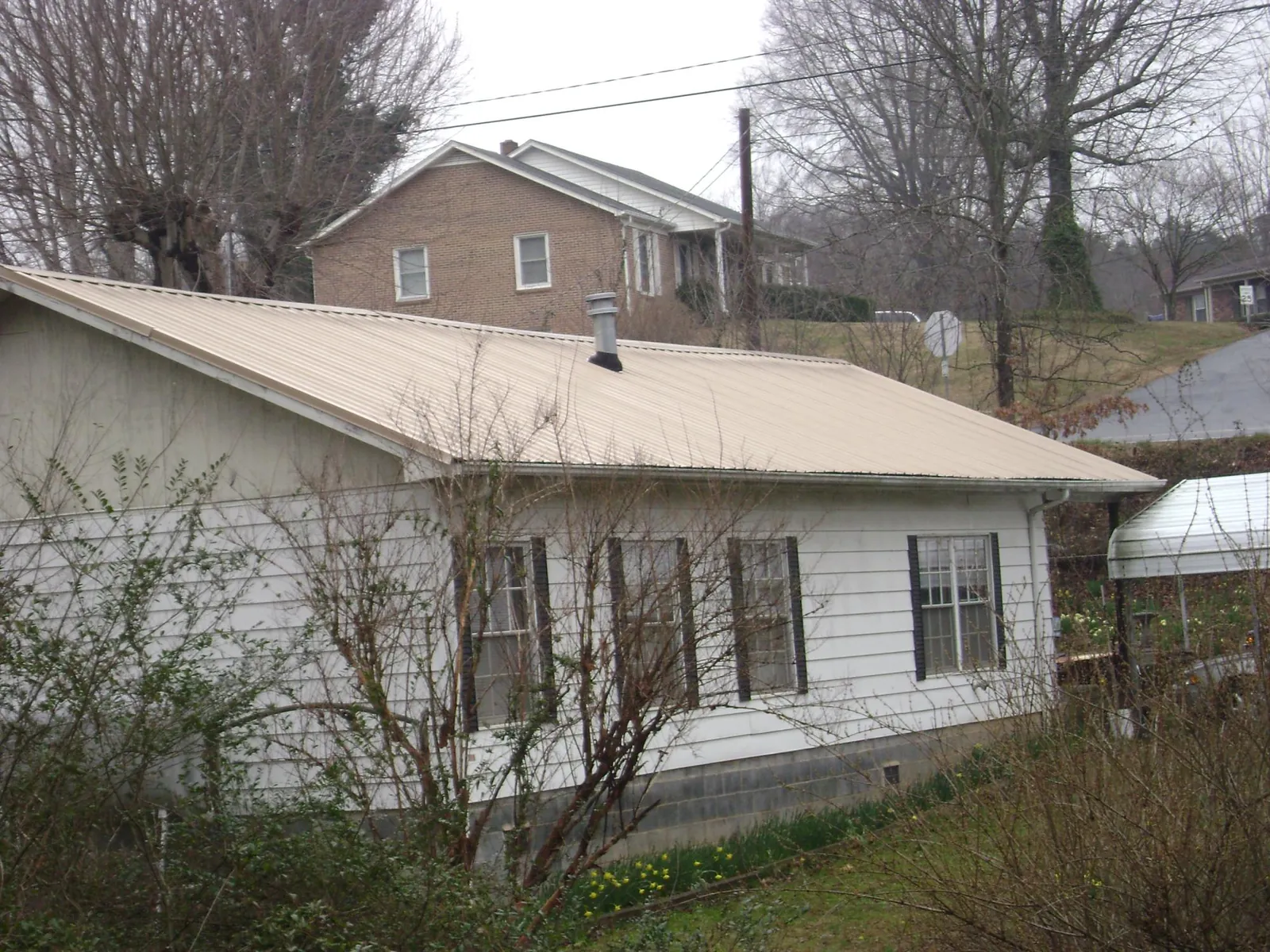 Tan metal roof on a white sided house set into a hillside — Commercial Roofing by Roofing Brothers in Issaquah